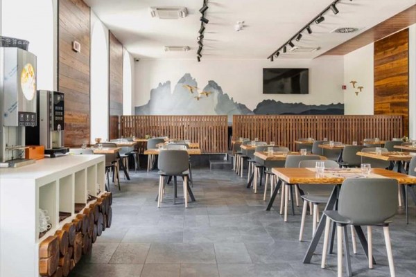 Nowoczesna restauracja z drewnianymi stołami i ścianą z przedstawieniem gór i ptaków.
