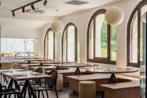 Nowoczesna restauracja z dużymi łukowymi oknami i okrągłymi stolikami.