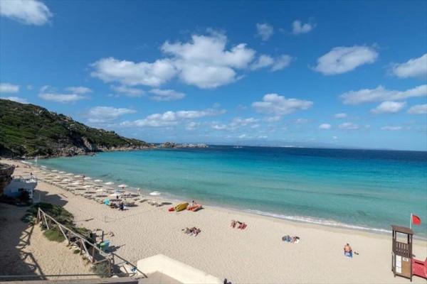 Piaszczysta plaża z leżakami i parasolami nad niebieskim morzem pod niebieskim niebem z chmurami.