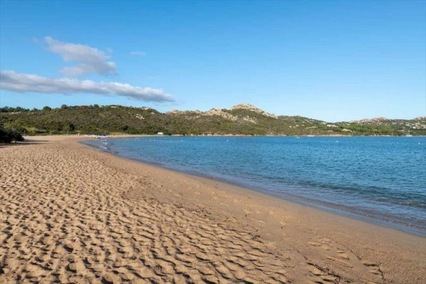 Piaszczysta plaża z widokiem na niebieskie morze i zielone wzgórza.
