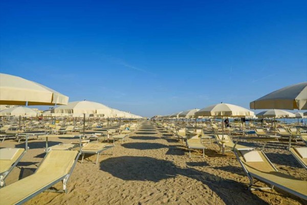 Piaszczysta plaża z rzędami pustych leżaków i parasoli pod niebieskim niebem.