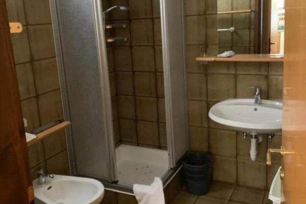 Łazienka z umywalką, kabiną prysznicową i bidetem na brązowych płytkach.