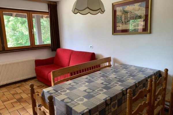 Pokój z czerwoną kanapą, drewnianym stołem i krzesłami, z oknem i zasłonami.