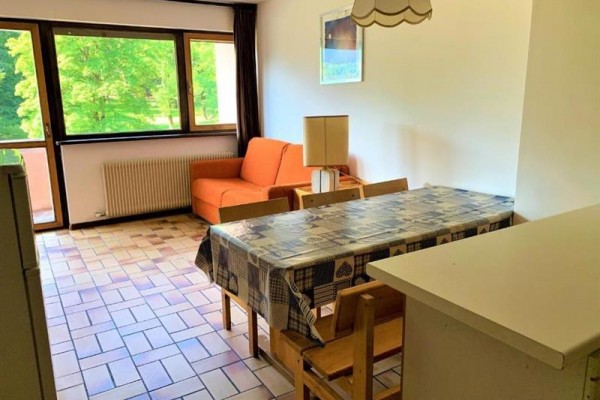 Słoneczny salon z pomarańczową kanapą, stołem jadalnym i dużymi oknami z widokiem na zieleń.