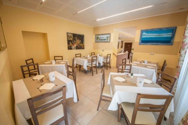 Jasna restauracja z drewnianymi krzesłami i stołami nakrytymi białymi obrusami.