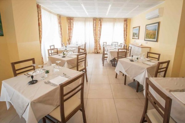 Jasna restauracja z kilkoma stołami nakrytymi białymi obrusami i drewnianymi krzesłami.