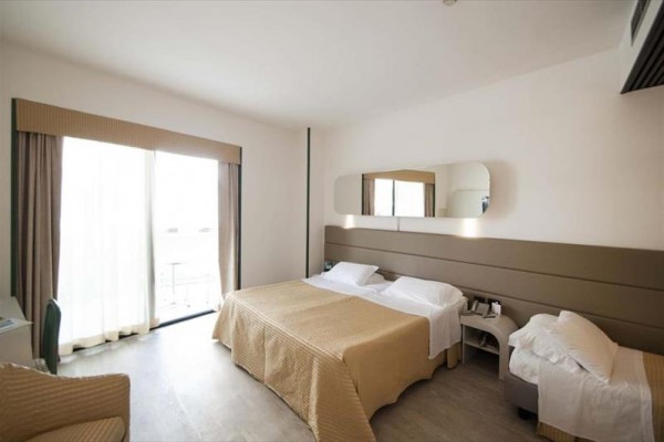 Jasny pokój hotelowy z łóżkiem małżeńskim i dostawką, oknem na balkon.