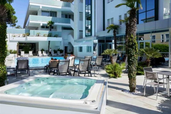 Nowoczesny hotel z basenem, wanną z hydromasażem i miejscem do siedzenia na zewnątrz otoczonym palmami.