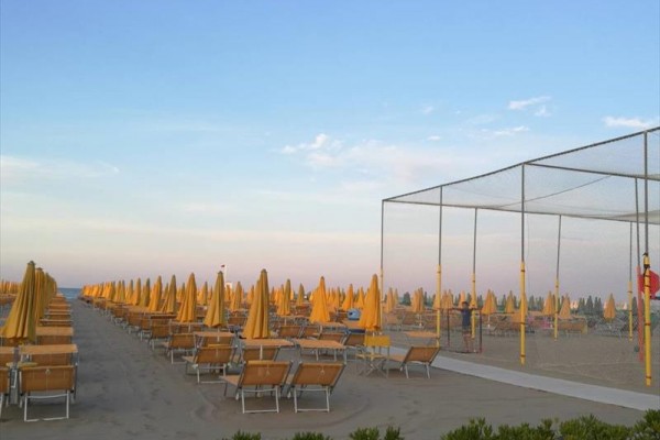 Rzędy pustych leżaków i parasoli na piaszczystej plaży podczas zachodu słońca.