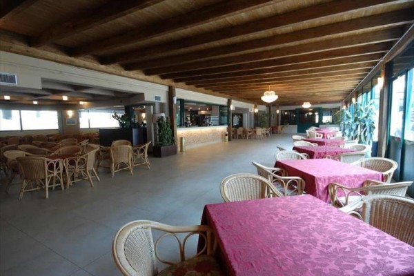 Duża restauracja z rattanowymi krzesłami i stołami z czerwonymi obrusami.