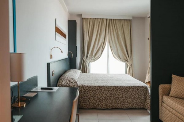 Pokój hotelowy z łóżkiem małżeńskim, biurkiem i zasłonami przed oknem.