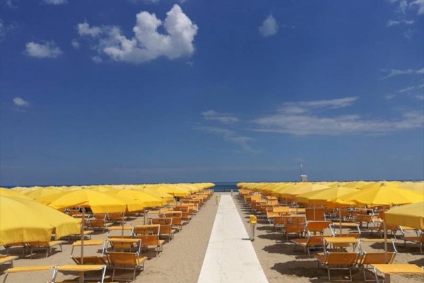 Plaża z żółtymi parasolami i leżakami pod niebieskim niebem.