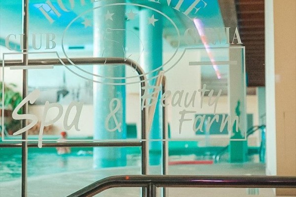 Szklane drzwi prowadzące do basenu z napisem Hotel Dante Spa & Beauty Farm.