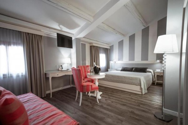Nowoczesny pokój hotelowy z podwójnym łóżkiem, białymi meblami i różowymi detalami.