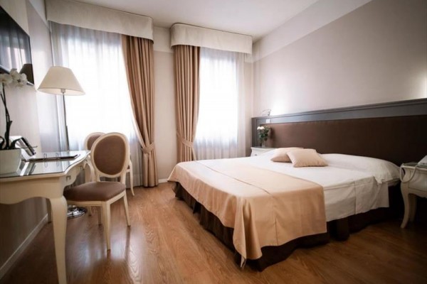 Elegancki pokój hotelowy z łóżkiem małżeńskim i meblami w kremowych odcieniach.