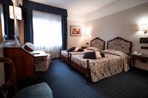 Pokój hotelowy z dwoma ozdobnymi łóżkami, biurkiem i fotelem.