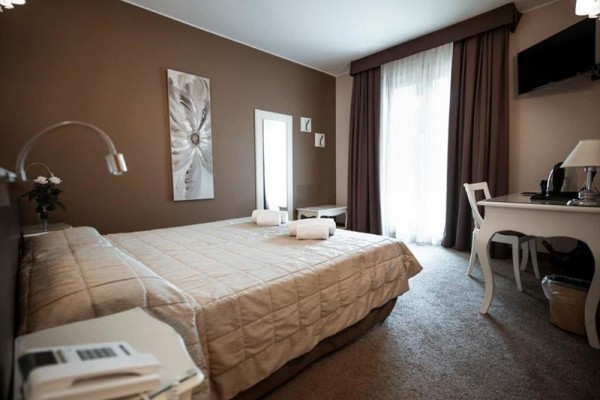 Nowocześnie urządzony pokój hotelowy z podwójnym łóżkiem, biurkiem, telewizorem i dużym oknem z ciemnymi zasłonami.