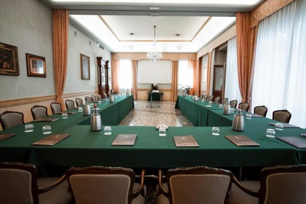 Sala konferencyjna z ustawieniem w kształcie litery U, zielonymi obrusami i krzesłami wokół stołów.