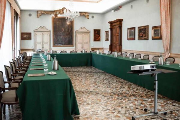 Sala konferencyjna z układem w kształcie litery U, zielonymi obrusami i projektorem.