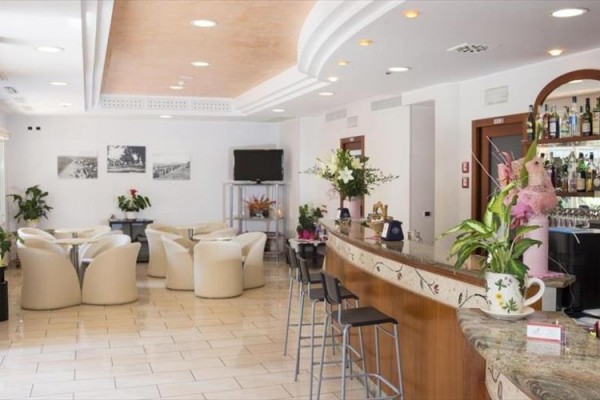 Elegancki bar hotelowy z białymi fotelami i kwiatowymi dekoracjami.