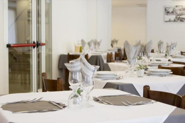Restauracja z elegancko nakrytymi stołami i białymi obrusami.