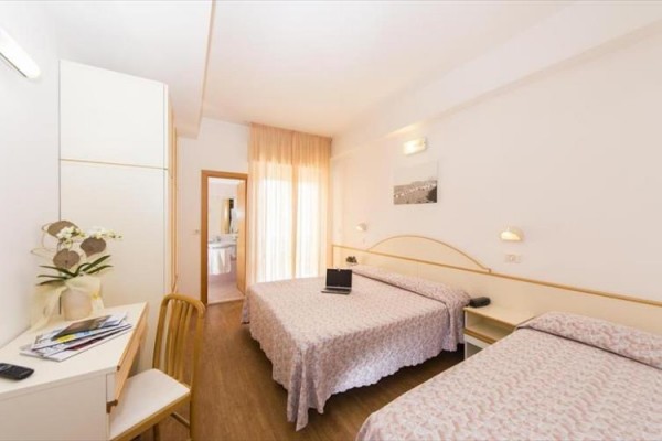 Pokój hotelowy z dwoma łóżkami, biurkiem z kwiatami i widokiem na łazienkę.