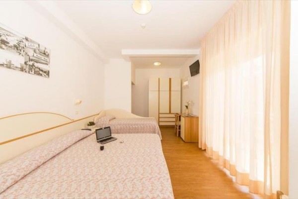 Jasny pokój hotelowy z dwoma łóżkami, biurkiem i płaskim telewizorem.