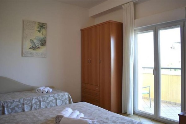Sypialnia z dwoma łóżkami, szafą i otwartymi drzwiami na balkon.