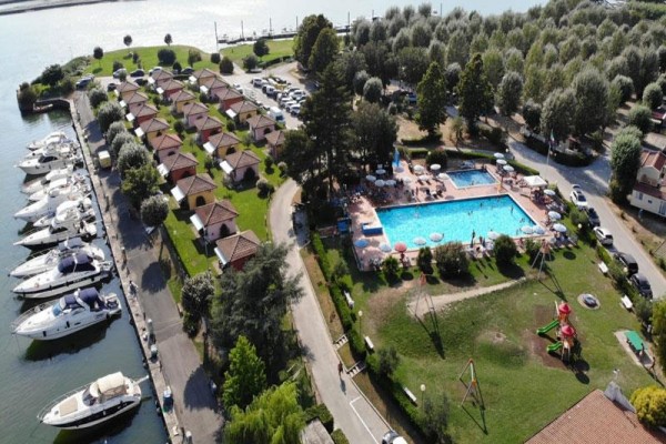 Widok z lotu ptaka na kemping z bungalowami, basenem i zacumowanymi łodziami przy wodzie.  