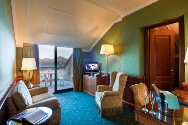 Elegancki pokój hotelowy z sofą, fotelami, telewizorem i balkonem z widokiem na góry.