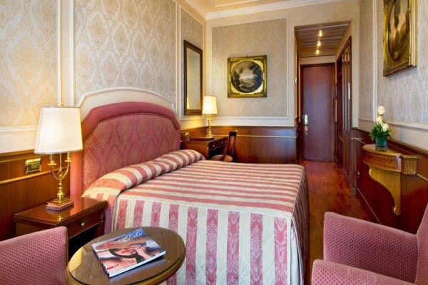 Elegancki pokój hotelowy z łóżkiem małżeńskim, obrazami na ścianach i drewnianymi meblami.