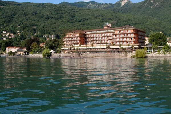 Duży hotel nad brzegiem jeziora z wzgórzami w tle.