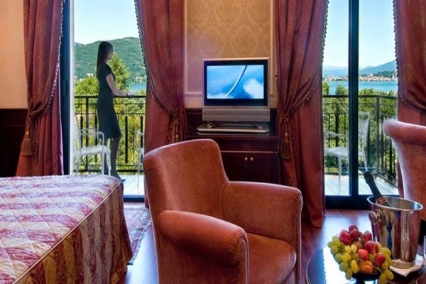Pokój hotelowy z balkonem, na którym stoi kobieta, z widokiem na jezioro.