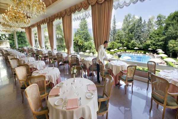 Elegancka restauracja z okrągłymi stolikami i widokiem na ogród z basenem.