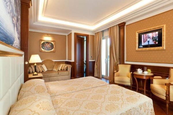 Elegancki pokój hotelowy z łóżkiem podwójnym, sofą i telewizorem na ścianie.