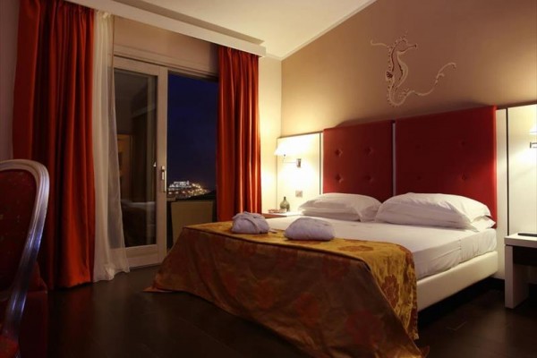 Luksusowo urządzona hotelowa sypialnia z podwójnym łóżkiem, widokiem z okna nocą i czerwonymi zasłonami.