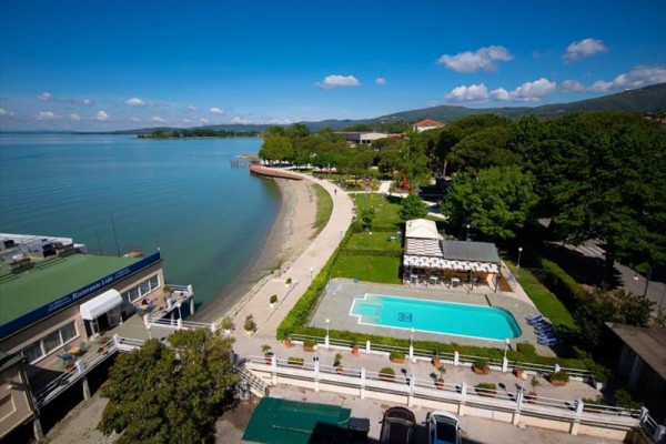 Widok na wybrzeże jeziora z plażą, basenem i otaczającą zielenią.