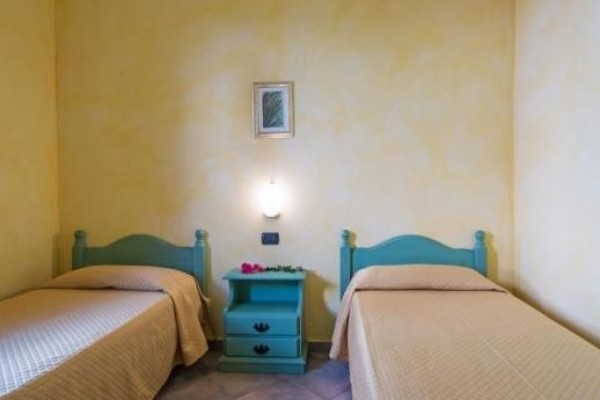 Dwa jednoosobowe łóżka z niebieskimi wezgłowiami i stolikiem nocnym pomiędzy nimi na żółtej ścianie.