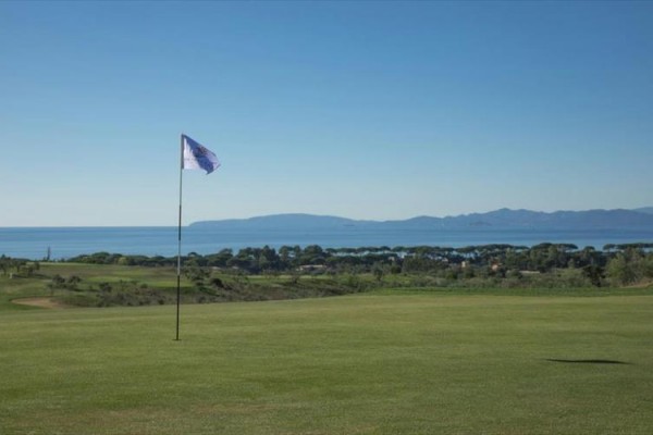 Pole golfowe z widokiem na morze i góry w tle.