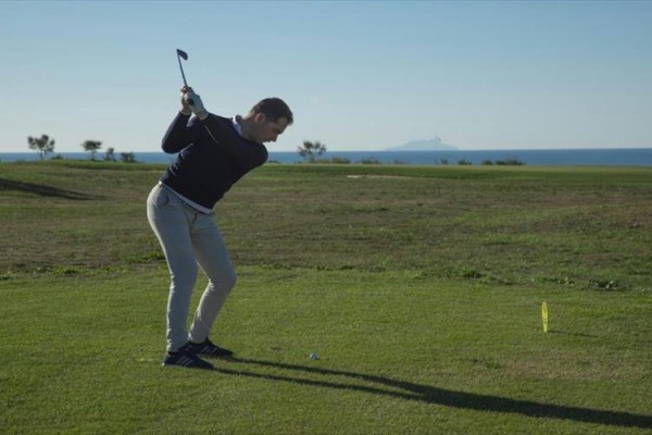 Mężczyzna na polu golfowym przygotowuje się do uderzenia piłki.