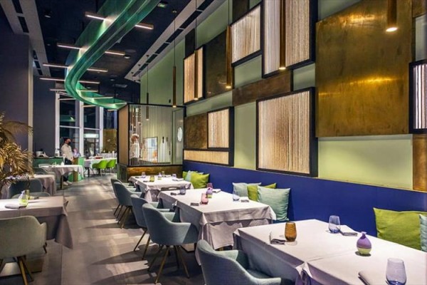 Nowoczesna restauracja z eleganckim układem stołów i kolorowym wnętrzem.  