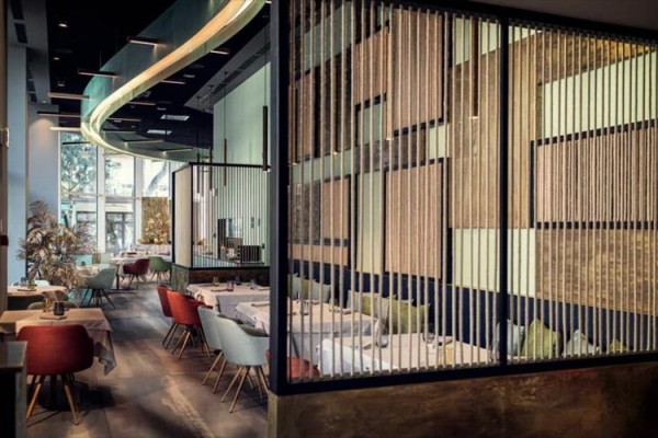 Nowoczesna restauracja z drewnianymi panelami oddzielającymi i kolorowymi krzesłami.