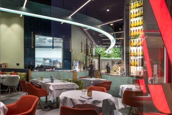 Nowoczesna restauracja z kolorowymi krzesłami i zakrzywioną instalacją świetlną.
