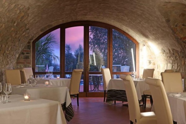 Wnętrze restauracji z łukowatymi oknami i widokiem na krajobraz o zachodzie słońca.