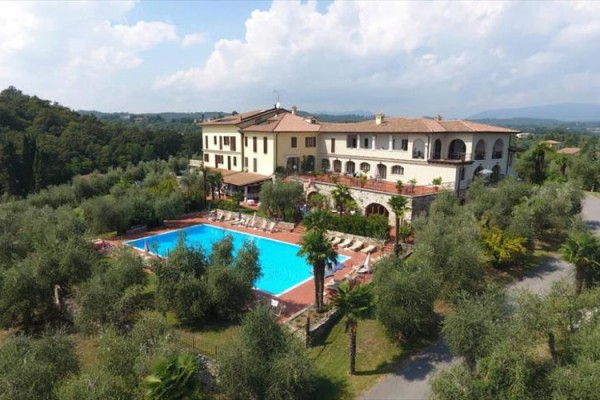 Hotel z basenem otoczony drzewkami oliwnymi i zielenią na wiejskim tle.