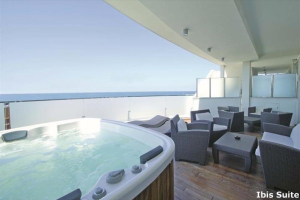 Taras z jacuzzi i rattanowym zestawem wypoczynkowym z widokiem na morze.