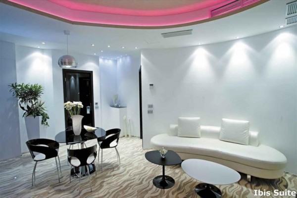 Nowoczesny salon z białymi meblami i różowym oświetleniem ambientowym.