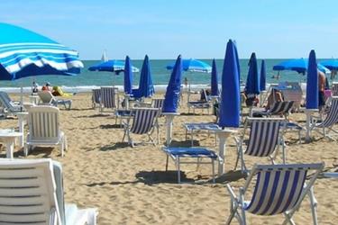 Plaża z niebieskimi parasolami i białymi leżakami nad morzem.