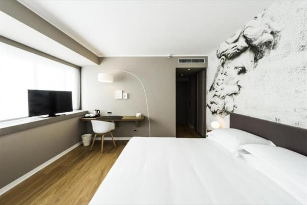 Nowoczesny pokój hotelowy z jasnym wystrojem i dużym łóżkiem.
