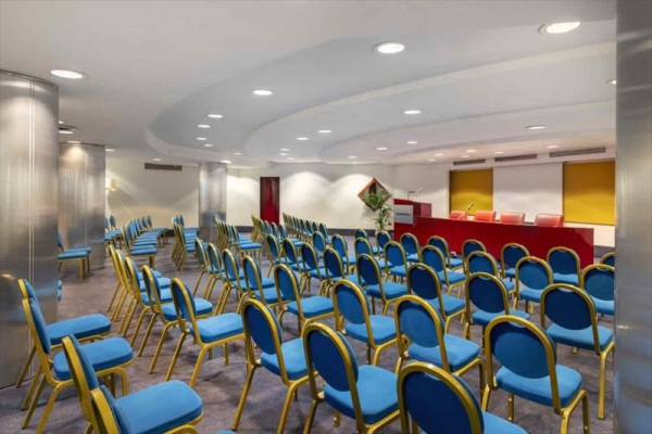 Sala konferencyjna z niebieskimi krzesłami i czerwoną sceną.